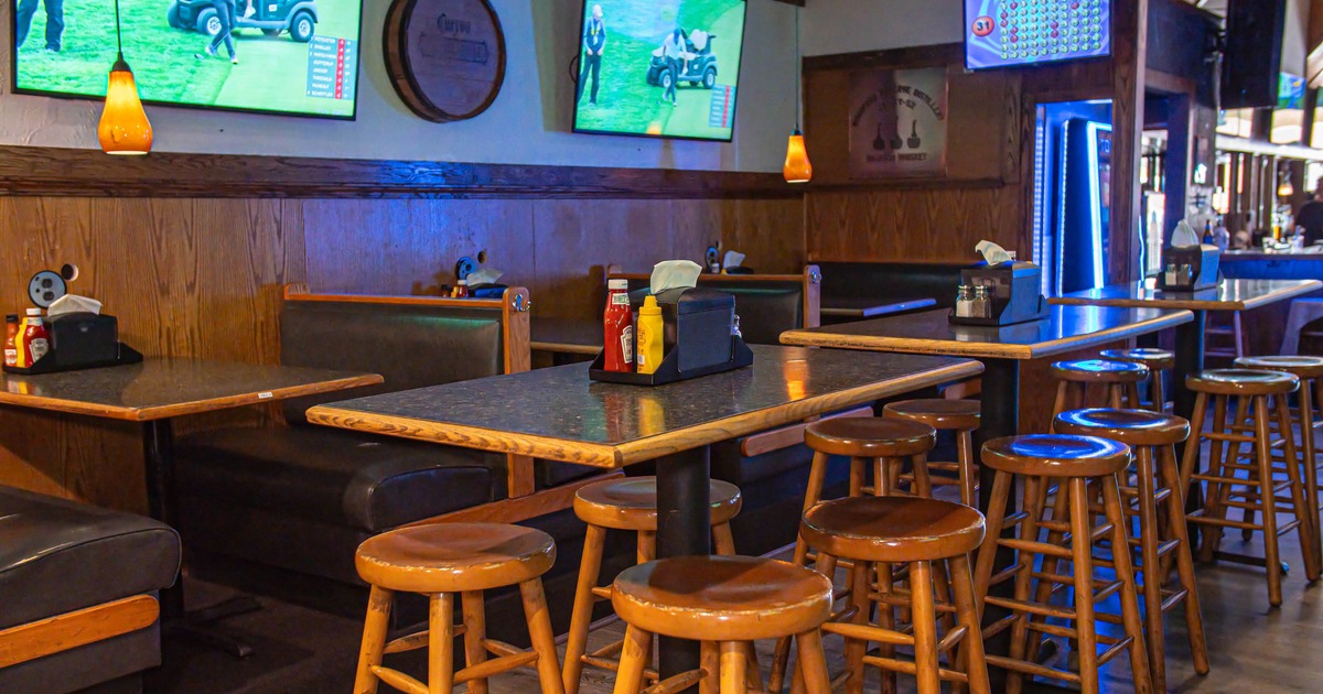 Interior - wooden stools, tables, booth seating and TVs showing a golf event.