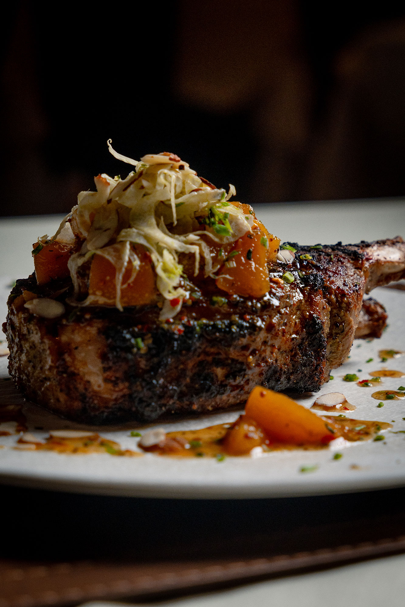 Our heritage pork chop from the menu, topped with braised, peach and fennel with sliced almonds on a white plate