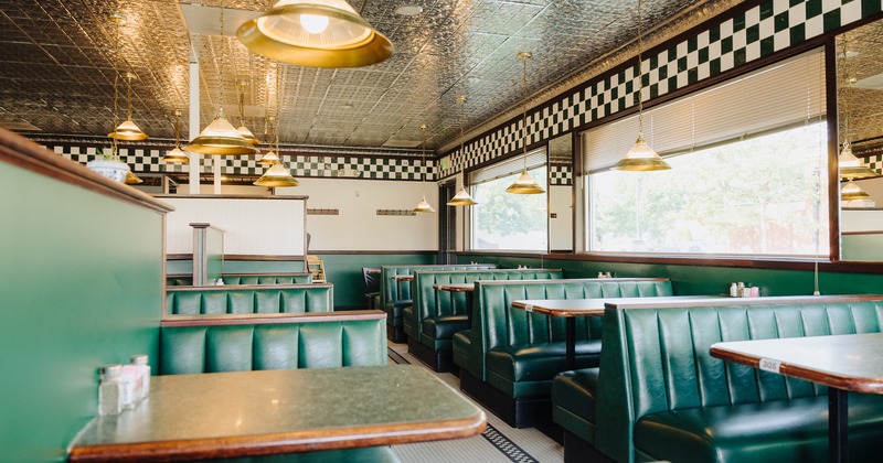 Interior, dining area with green walls, large windows and green upholstered booths