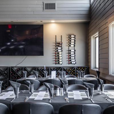 Modern dining room with black table settings, wine display, and wall television.