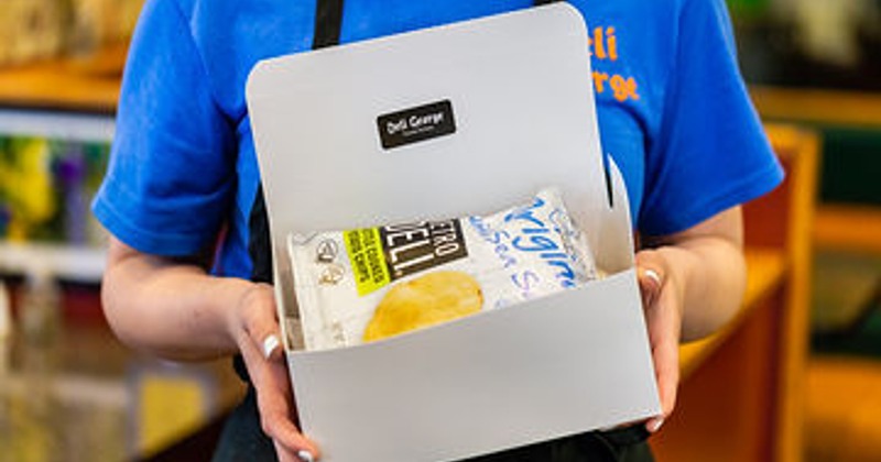 An employee holding a lunch box with a bag of chips in a restaurant