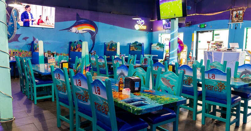 Interior of a marine-themed restaurant with turquoise furniture, marine murals, and two televisions
