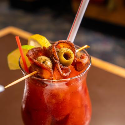 Bloody Mary cocktail garnished with bacon and olives on a pick.