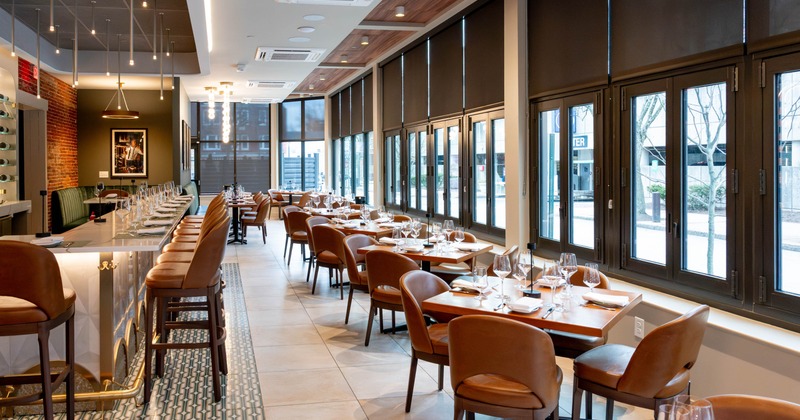 Modern restaurant interior with a marble-topped bar and neatly arranged tables by large windows