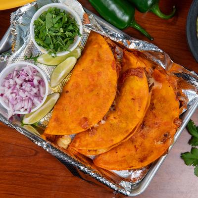 Quesabirria tacos served with cilantro, chopped red onions, and lime wedges.