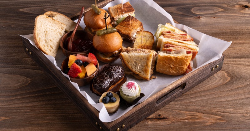 A platter with small sliders, sandwiches, jam, fruits, and desserts