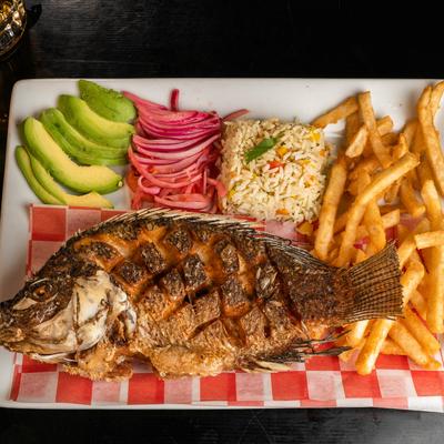 Whole fried tilapia served with fries, rice, sliced avocado, and pickled red onions.