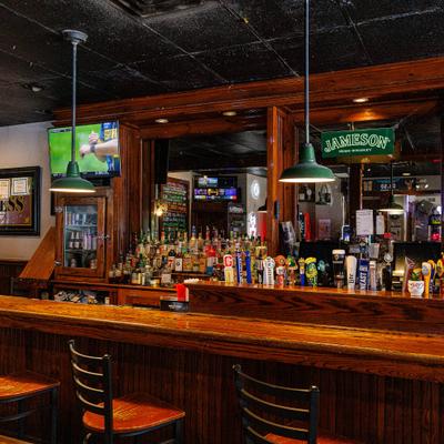 A traditional wooden bar counter featuring liquor shelves and hanging green pendant lights.