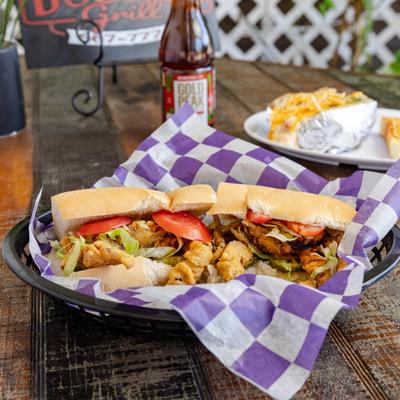 Soft Shell Crab Po-boy served alongside plate with loaded potato and botteled drink.