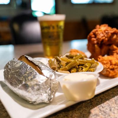Baked potato with green beans, fried chicken, sour cream, and a beer in the background.