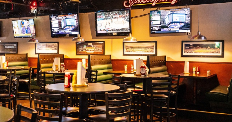 Interior, tables and chairs, and booths along the wall with TV screens above