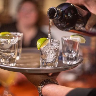 Server pouring tequila shots on a tray, garnished with lime and salt.