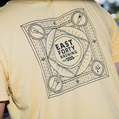 The back of a pale yellow T-shirt - a black geometric brewing graphic labeled EAST FORTY BREWING.