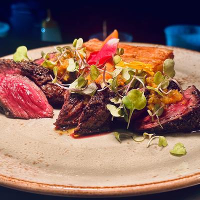 Sliced medium-rare steak served with microgreens and cornbread.