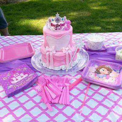 A pink princess-themed birthday cake sits on a table set with pink utensils, napkins, and plates.