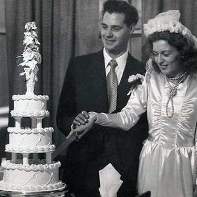 Vintage wedding photo of a bride and a groom cutting a multi-tiered wedding cake.