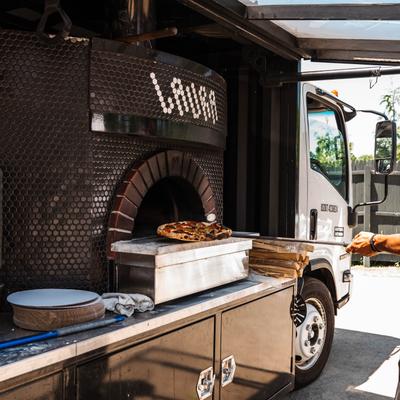 A person removing a pizza from a brick oven using a pizza peel.