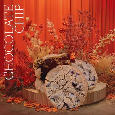 Chocolate chip cookies displayed with autumnal flowers and orange backdrop.