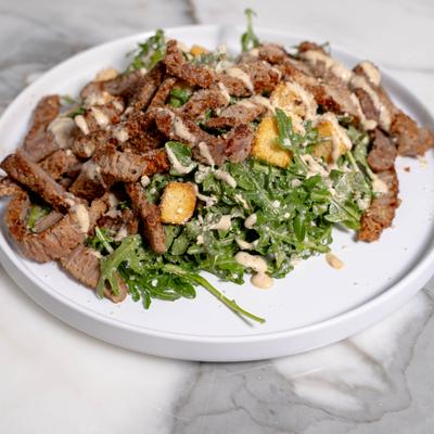 Steak and arugula salad with croutons and a drizzle of sauce.