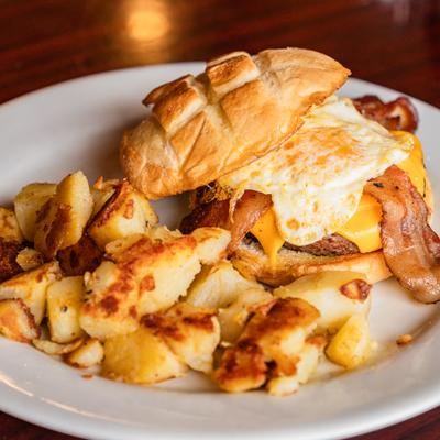 A breakfast burger with beef patty, egg, bacon, and cheddar, served with potatoes.