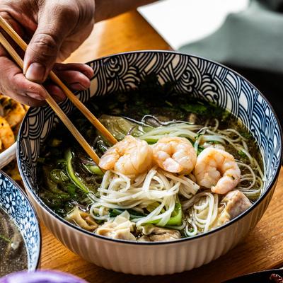 Wonton pho, a hand mixing the pho with chopsticks, closeup