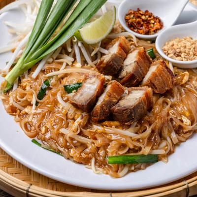 Pad Thai noodles topped with crispy pork belly, lime, scallions, and side spices.