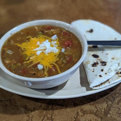 Bowl of green chile served with tortilla.