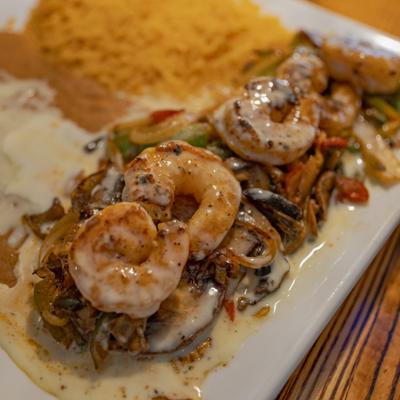 Grilled steak topped with shrimp, onions, and bell peppers, served with rice and beans.