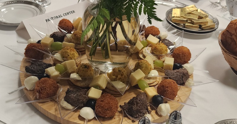 Round board with assorted foods, such as cheese and rice balls, on a set table