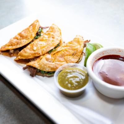 Quesabirria tacos served alongside dipping sauces.