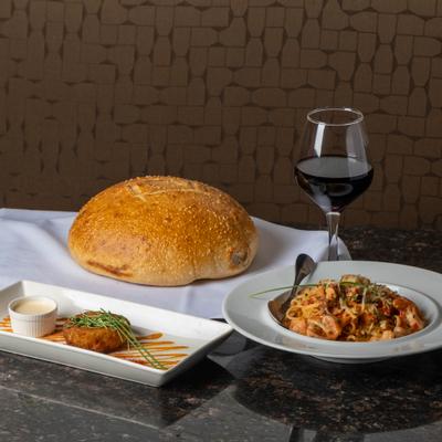 Bread loaf, wine glass, crab cake, and pasta on table.