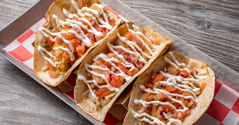 Fish and shrimp tacos topped with sauce and diced tomatoes