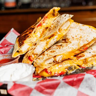 Chicken Quesadilla served in a red-and-white checkered basket with salsa and sour cream.