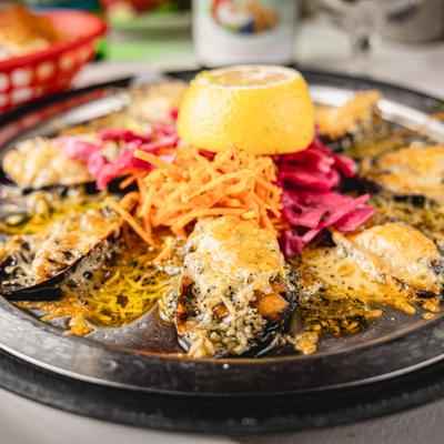 A dish of baked mussels served on a metal platter with a lemon half and pickled vegetables.