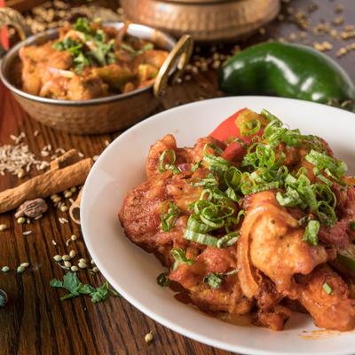 Indian butter chicken with sliced peppers and green onions, other dishes in the background.