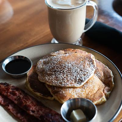 Pancake and bacon breakfast served with coffee beverage.
