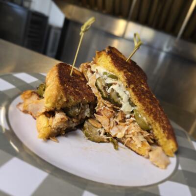 A sandwich with shredded chicken, melted cheese, and jalapenos.