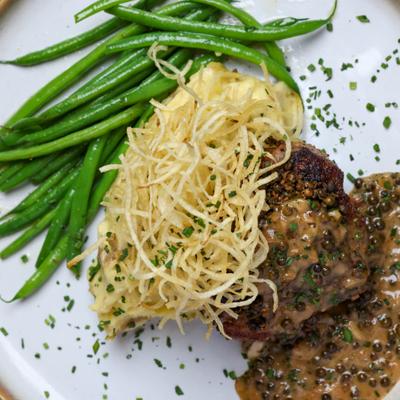 Steak topped with creamy peppercorn sauce, served with shoestring potatoes and green beans.