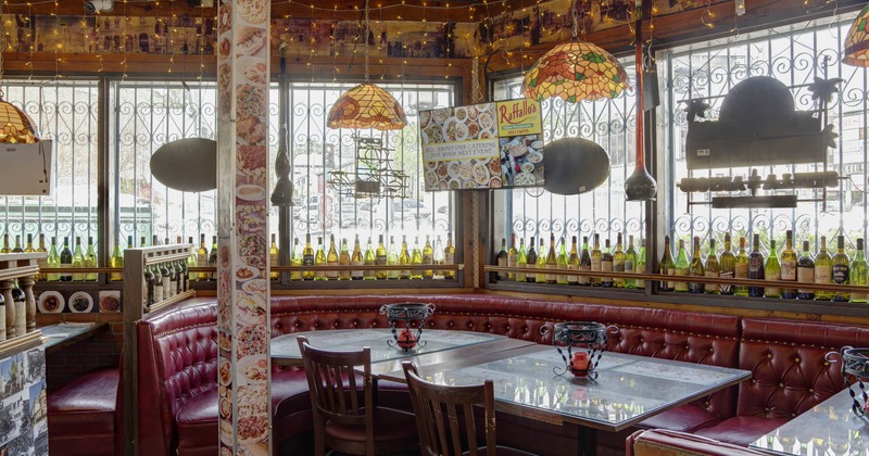 Interior with dark red leather booths, wine bottles on the windowsill, and stained glass pendant lights