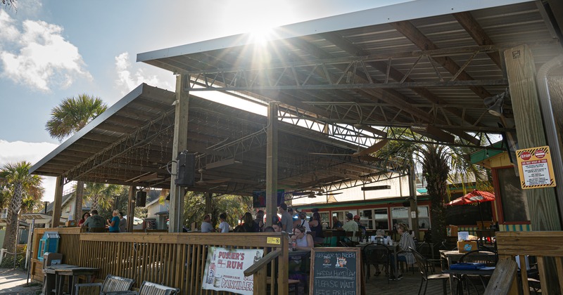 Exterior, covered seating area, tables, chairs, benches, customers, tropical trees
