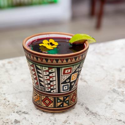 Peruvian purple corn drink with lime and edible flower garnish served in a clay mug.