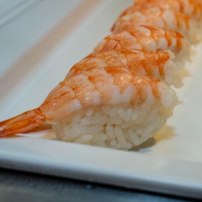 A row of shrimp nigiri sushi rests on a white rectangular plate.