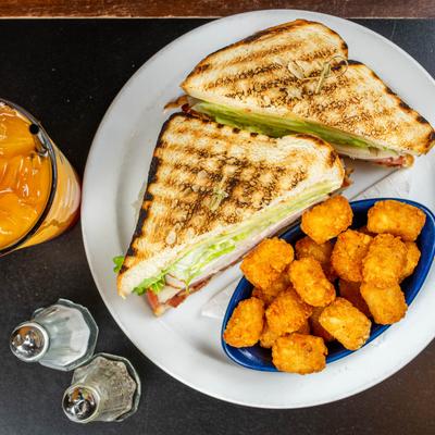Top view of the Turkey club sandwich with a side of tots.