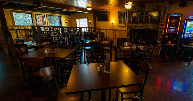 Dining room with wooden tables, a brick fireplace, wall sign, and illuminated gaming machines
