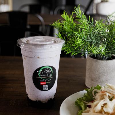 A cold beverage in a branded plastic cup next to a plant.