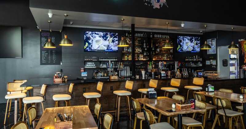 Interior, wooden counter, woven chairs, pendant lights, two TVs, and tables with chairs