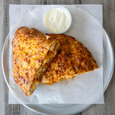 Buffalo chicken calzone with a cup of ranch sauce.