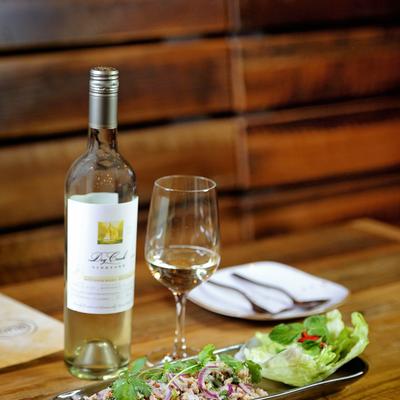 A bottle of white wine with a half-full glass next to a salad.