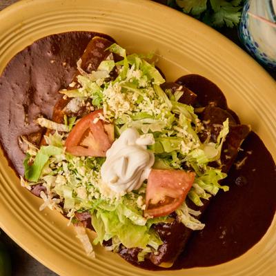 Enchiladas with mole sauce, lettuce, tomatoes, cheese, and sour cream on a yellow plate.