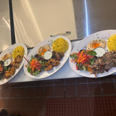 Three plates with rice salad grilled meat on counter.